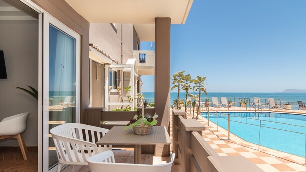 Un balcon avec une piscine, des chaises blanches et une table sur laquelle se trouve un panier de raisins.