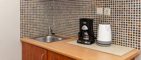 Una cocina con salpicadero de azulejos, una cafetera y un hervidor sobre la encimera.