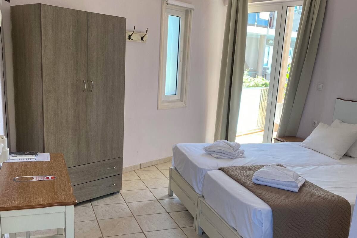 A bedroom with a bed, a desk, a wardrobe, and a window with curtains.