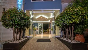 Un bâtiment moderne avec une entrée en verre, des arbres en pot et un chemin dallé menant à la porte.