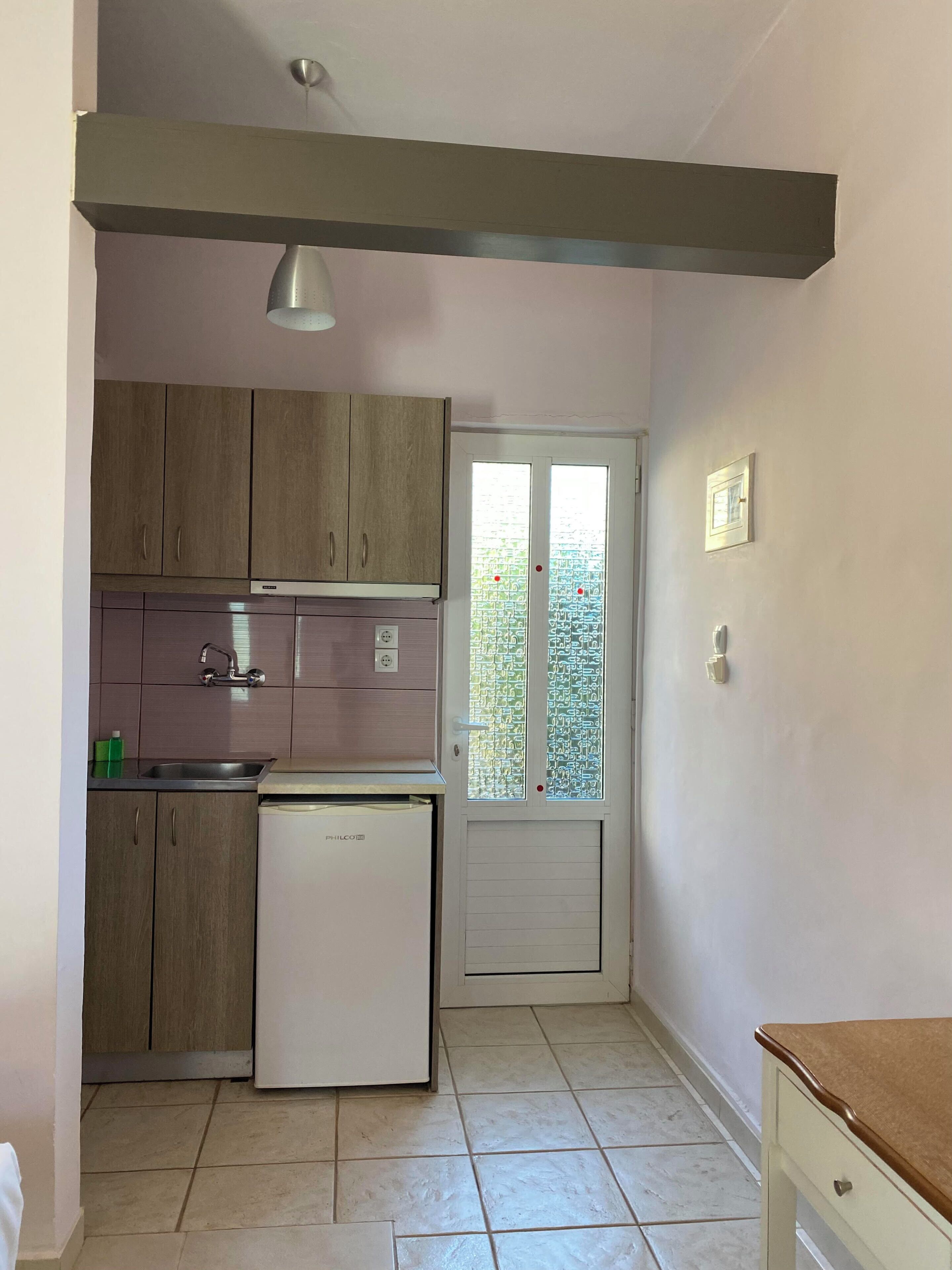 A compact kitchen with wooden cabinets, a built-in sink, a small refrigerator, and a window with a view.