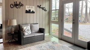 A cozy living room with a wicker sofa, a lamp, and wall decor featuring city names and a skyline silhouette. - Cozy Cottage Wooded Retreat (Hendersonville)