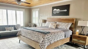 A bedroom with a large bed, a wooden headboard, a nightstand with a lamp, and a wall-mounted artwork. - Cozy Cottage Wooded Retreat (Hendersonville)