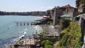A coastal town with a stone pier extending into the sea, a rocky beach, and buildings with balconies overlooking the water. - The great view and the perfect leisure time (Sozopol)