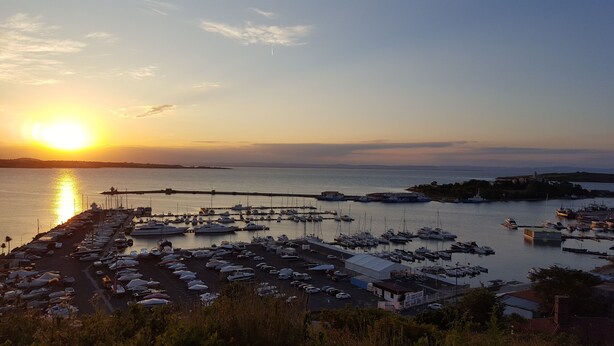 A marina at sunset with boats docked, a pier extending into the water, and buildings in the background. - The great view and the perfect leisure time (Sozopol)