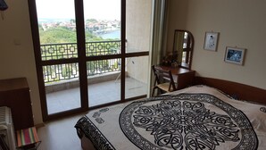 A hotel room with a large window offering a city view, a bed with a patterned bedspread, a desk with a chair, and a mirror on the wall. - The great view and the perfect leisure time (Sozopol)