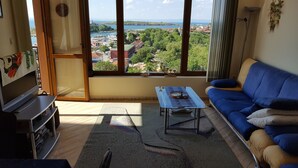 A living room with a large window, a blue sofa, a coffee table, and a television. - The great view and the perfect leisure time (Sozopol)