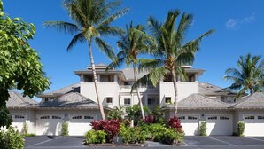 A multi-story residential building with a symmetrical facade, multiple garage doors, and a landscaped front yard with palm trees and shrubs. - Hilton Pool Pass for stays 2026. Golf Discounts. Waikoloa Beach Villas L22 (Waikoloa Beach Resort)