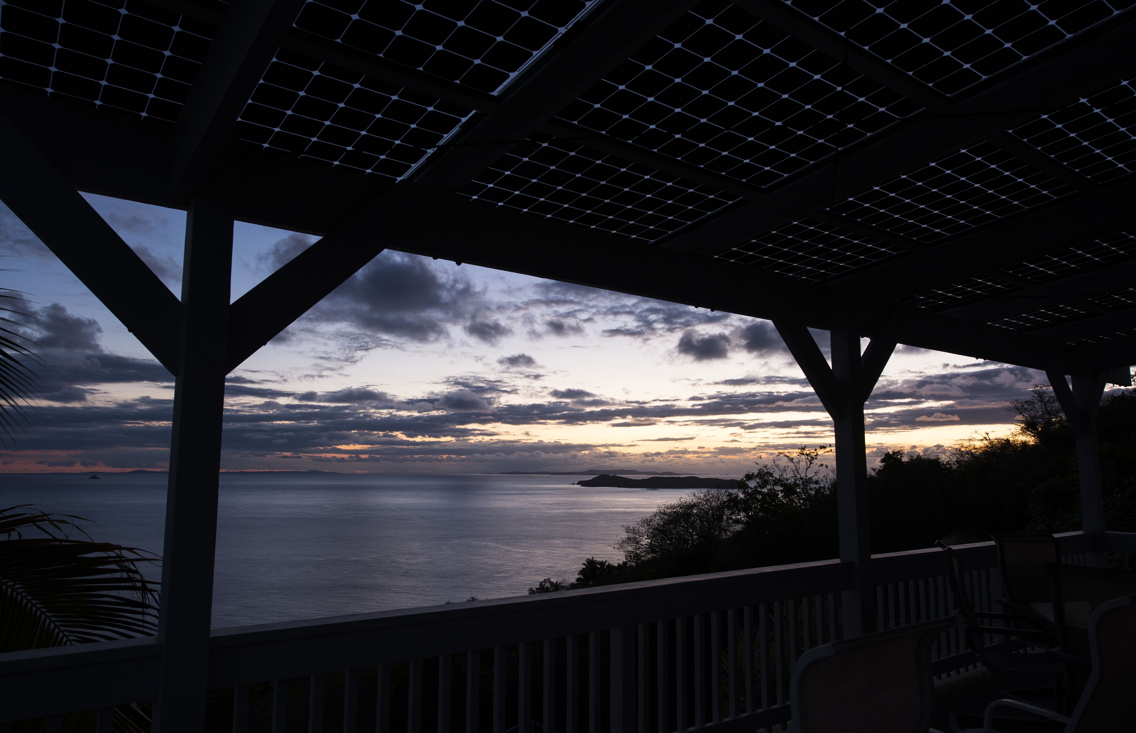 Ein überdachter Außenbereich mit Blick auf das Meer und einen Sonnenuntergang.