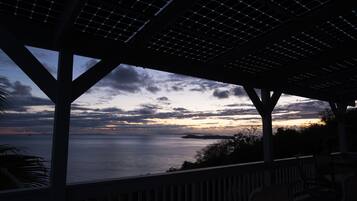 Ein überdachter Außenbereich mit Blick auf das Meer und einen Sonnenuntergang.