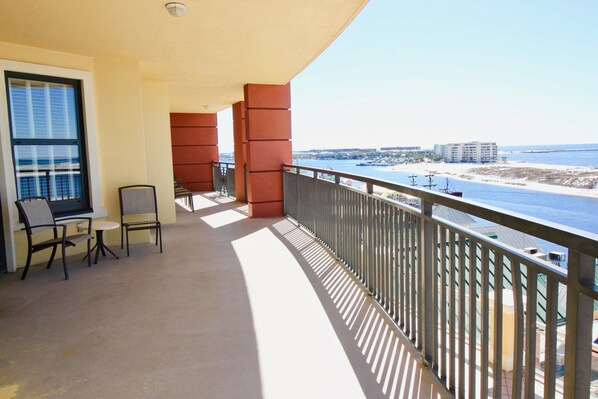 A balcony with a view of the beach and ocean, featuring a table and chairs, and a railing. - CORNER UNIT WRAPAROUND BALCONY. Amazing views! See description for dates avail! (Destin)