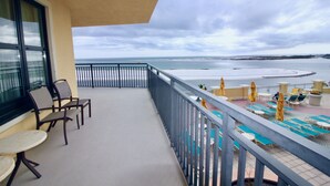 En balkong med utsikt över stranden, utomhusmöbler och ett poolområde.