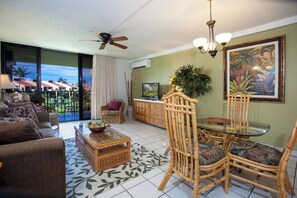 A spacious living room with a balcony, a ceiling fan, a television, and a dining area with wicker furniture.