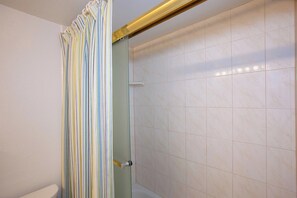 A shower with a glass door, tiled walls, and a curtain with vertical stripes.