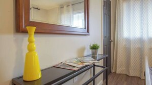 A hallway with a black console table, a yellow vase, and a mirror reflecting a window with curtains.