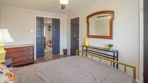 A bedroom with a bed, a ceiling fan, a dresser, a mirror, and a desk with a plant.