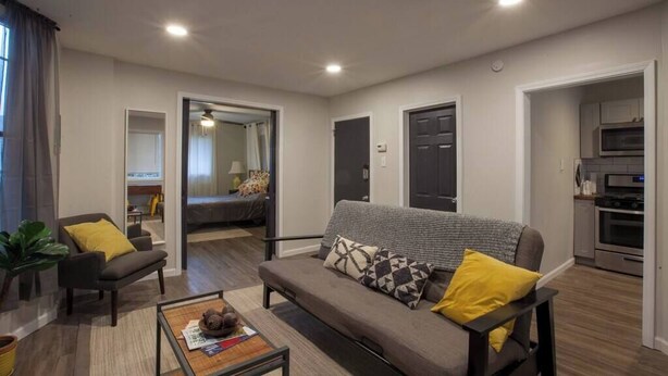 A modern living room with a sofa, armchairs, and a coffee table. There is a kitchen area with a microwave and oven.