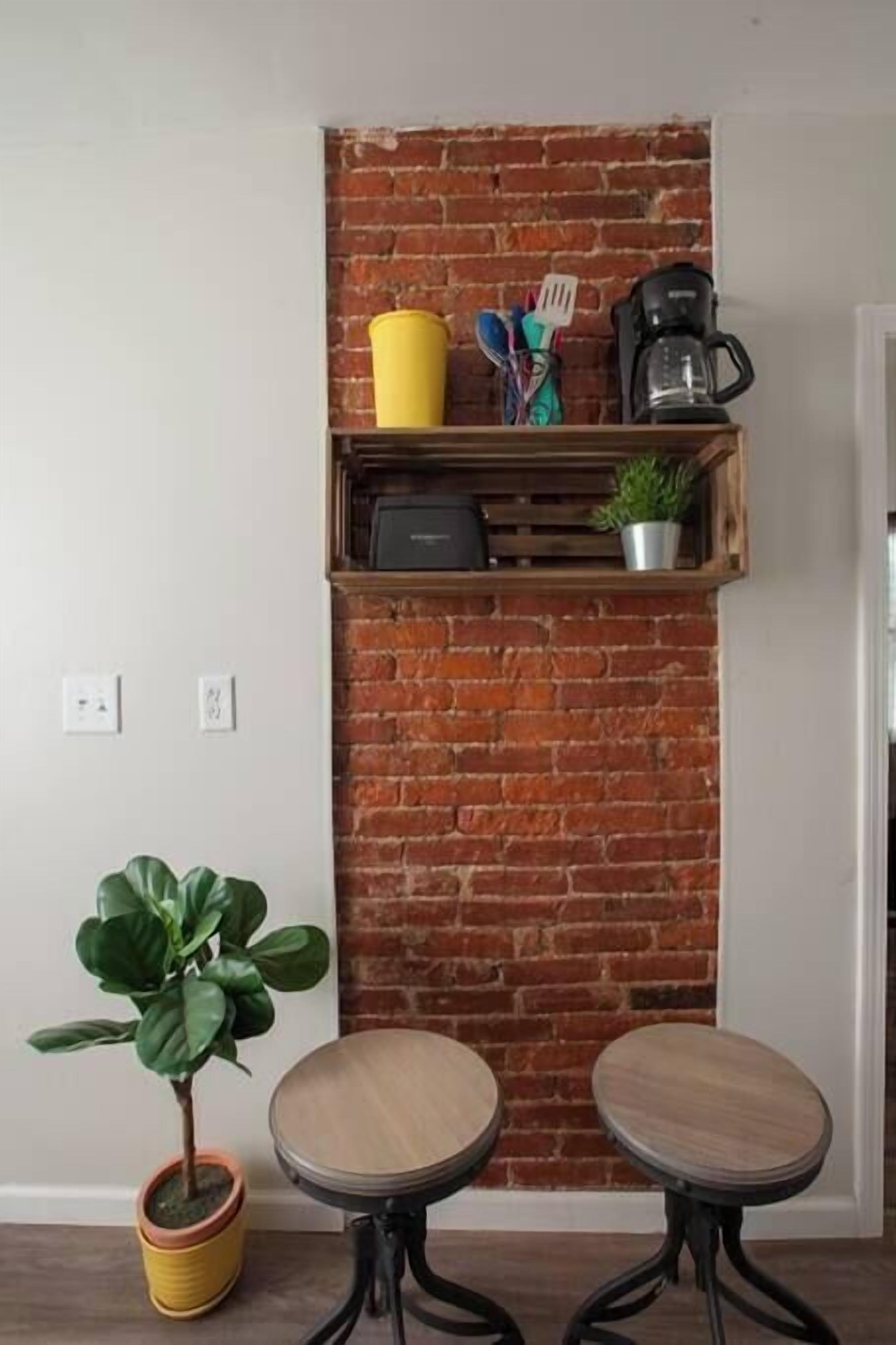 Une pièce avec un mur d’accent en briques, deux tables rondes, une plante en pot et une étagère contenant des ustensiles de cuisine.