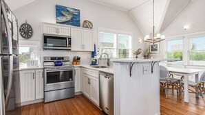 A kitchen with white cabinetry, stainless steel appliances, a dining area with wicker chairs, and a view of the outdoors.