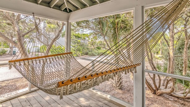 A hammock in a covered outdoor area with wooden flooring and large windows.