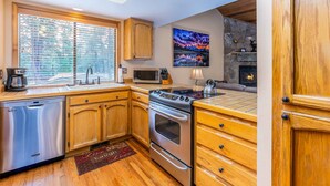 A modern kitchen with wooden cabinets, stainless steel appliances, and a large window with blinds. - ASHW05 - Charming Home, A/C, Hot Tub,  Bikes (Sunriver)