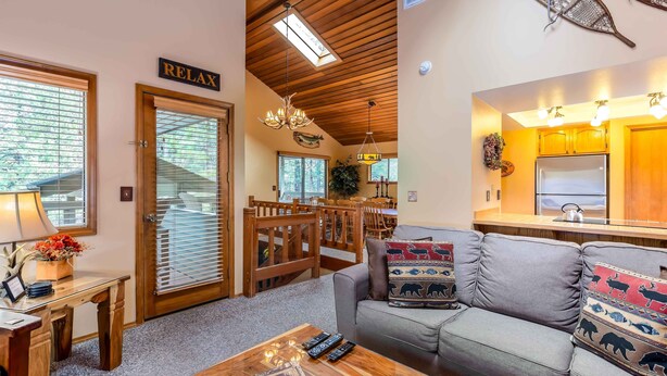 A cozy living room with a sofa, wooden coffee table, and a dining area with a table and chairs. - ASHW05 - Charming Home, A/C, Hot Tub,  Bikes (Sunriver)