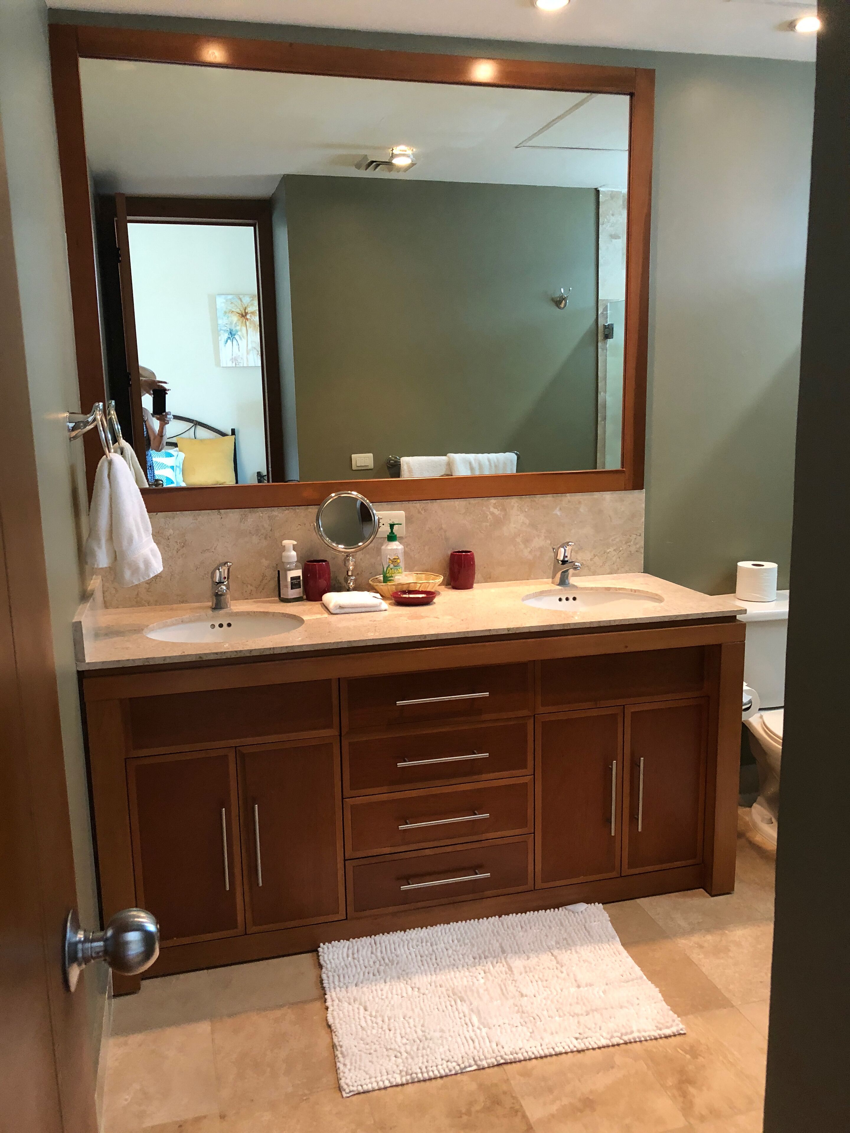 A bathroom with a double sink vanity, a large mirror, and a white bath mat.