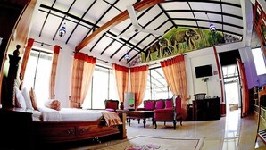 Um quarto amplo com uma cama grande, área de estar com cadeiras e teto com estrutura de vigas de madeira.