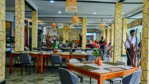Um restaurante com mesas e cadeiras, luminárias pendentes e uma geladeira Coca-Cola ao fundo.