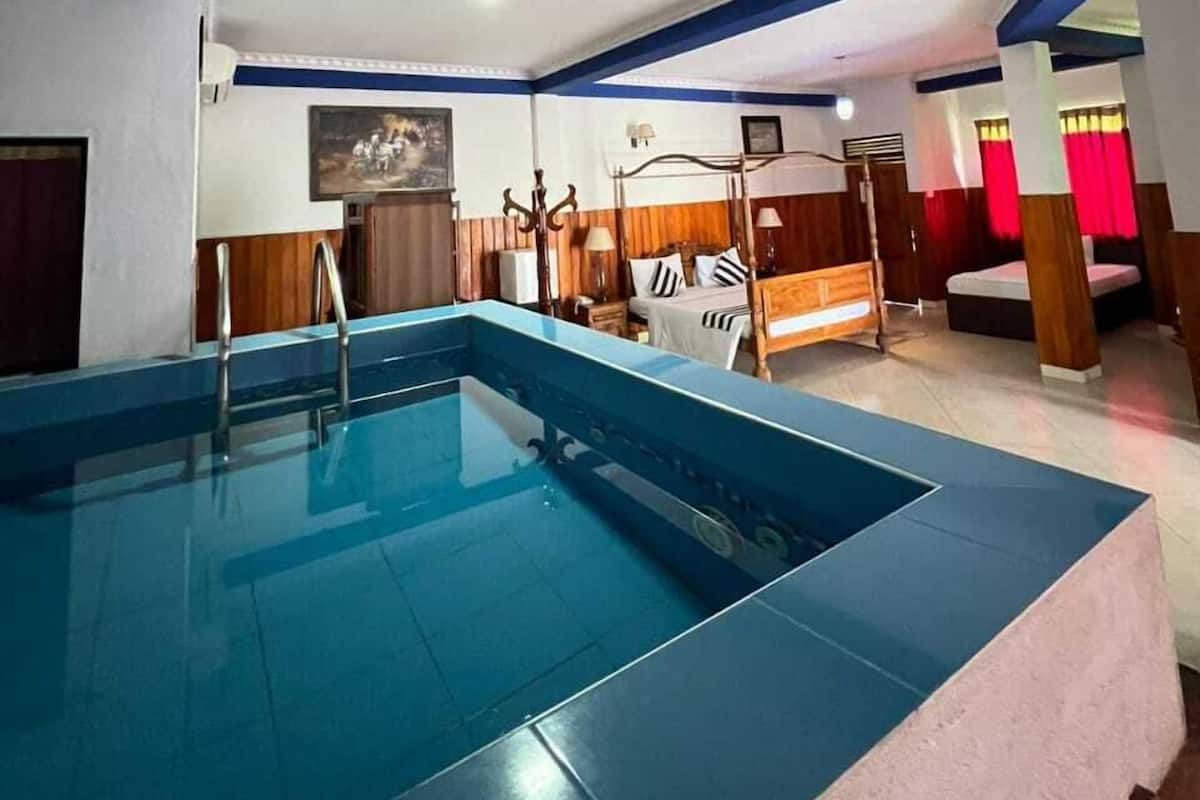 Quarto de hotel com uma piscina grande, móveis de madeira e uma cama com cabeceira.