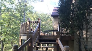 Eine Holztreppe führt zu einem Gebäude mit rotem Dach, umgeben von Bäumen.