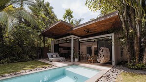 Una moderna casa con piscina, terrazza in legno e vegetazione lussureggiante.