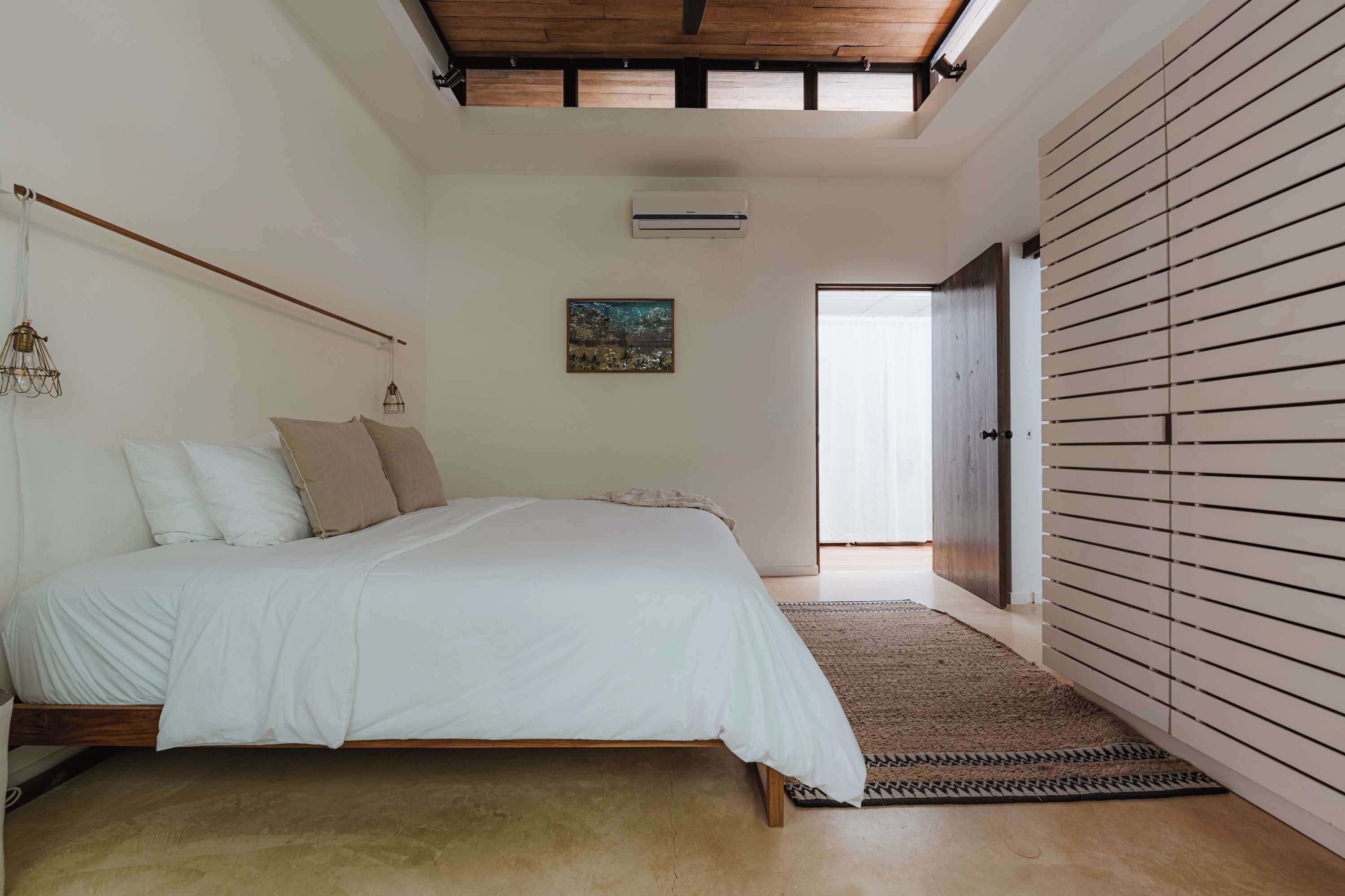 Een slaapkamer met een bed, een hanglamp, een airconditioning en een deur naar een andere kamer.