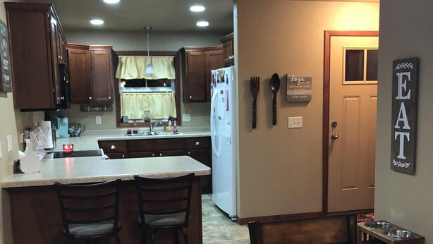 Una cocina con armarios de madera, un refrigerador, una mesa de comedor con sillas y un letrero que dice 'EAT'.