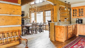 Een landelijke keuken met houten kastjes, een eethoek met een houten bank, en een kroonluchter.