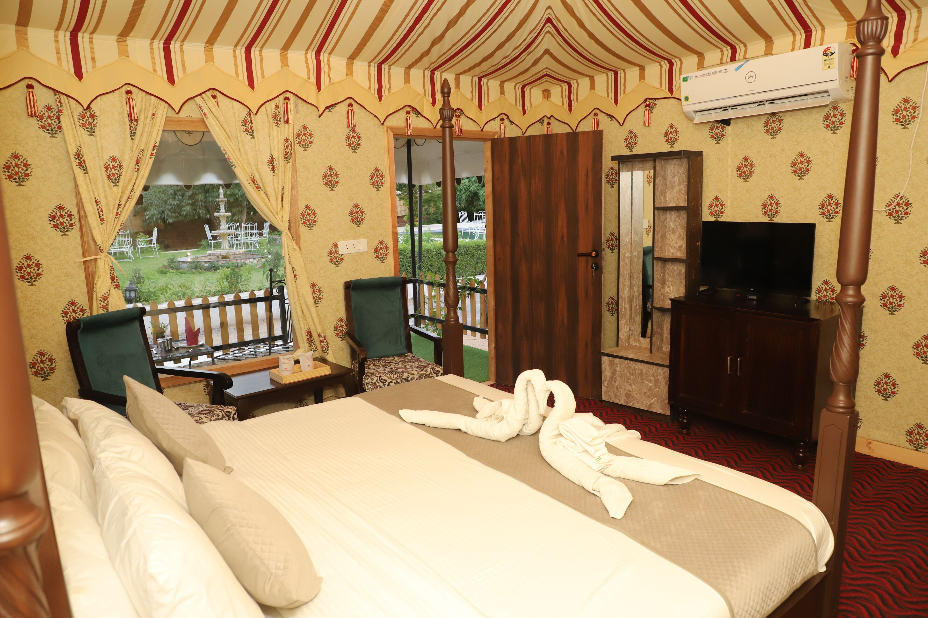 Een hotelkamer met een hemelbed, een televisie, een garderobe en een balkon met uitzicht op de tuin.