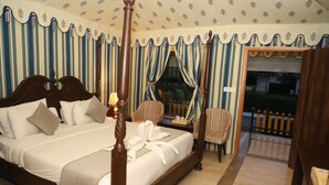 Ein Himmelbett mit Baldachin, ein Nachttisch mit Lampe, gestreifte Vorhänge und Blick auf einen umzäunten Garten.