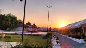 Ein Weg, der zu traditionellen Gebäuden führt, mit einem Sonnenuntergang im Hintergrund.