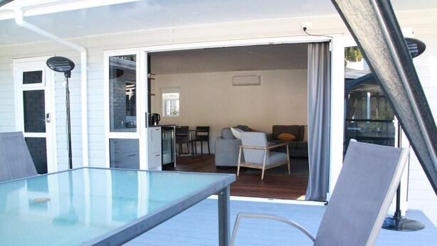 A deck with a glass table and chairs, a kitchen area with a coffee machine, and a living room with a sofa and chairs.