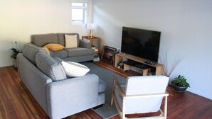 A living room with a grey sofa, a white armchair, a flat-screen TV, and a wooden coffee table.
