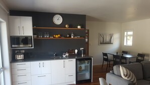 A compact kitchen with a microwave, toaster, and refrigerator, a dining area with a table and chairs, and a living area with a sofa and a coffee table.