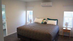 A bedroom with a large bed, a nightstand, a window, and an air conditioning unit.
