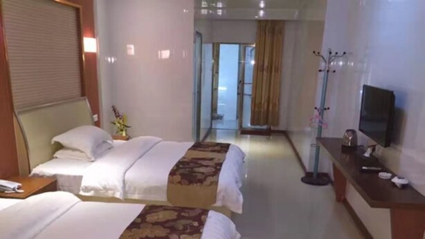 Habitación de hotel con dos camas, un escritorio con televisor y un pasillo que lleva a un baño.