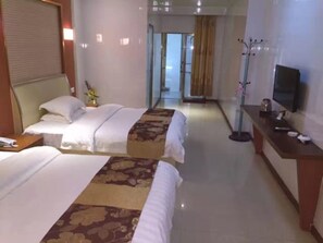 Habitación de hotel con dos camas, un escritorio con televisor y un pasillo que lleva a un baño.