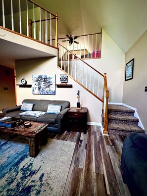 A living room with a staircase, a ceiling fan, a clock, and a coffee table.