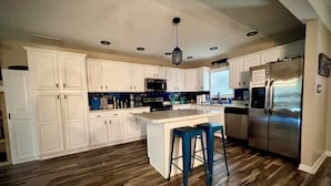Una cocina con armarios blancos, un refrigerador de acero inoxidable y piso de madera.