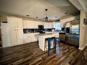A kitchen with white cabinets, a stainless steel refrigerator, and a wooden floor.