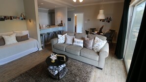 A living room with a sofa, coffee table, and a ceiling fan. There is a kitchen area in the background with a dining table and chairs. - Lakefront Walkout Condo in StillWaters – Stunning Views & Prime Location! (Dadeville)