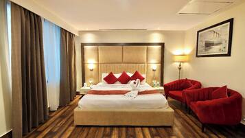 Habitación de hotel con una cama grande, sillas rojas, un cuadro en la pared y suelo de madera.