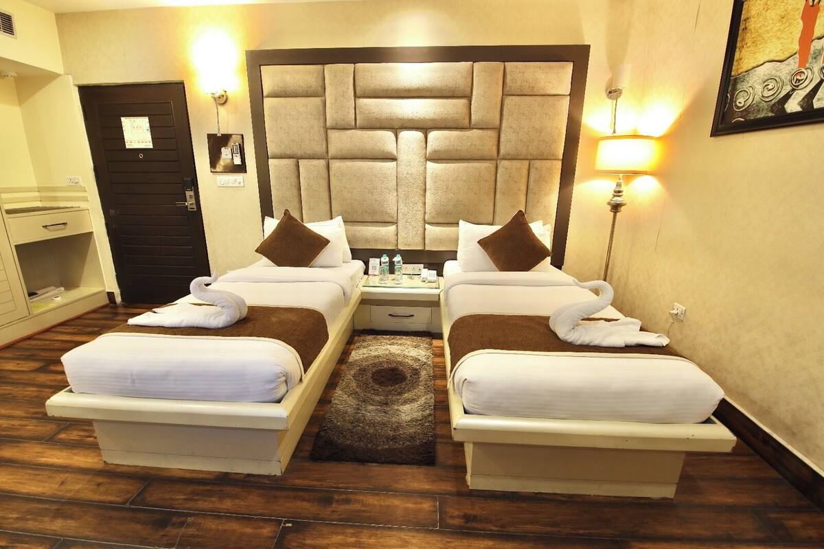 A hotel room with two beds, a headboard, bedside lamps, a small table, and a door.